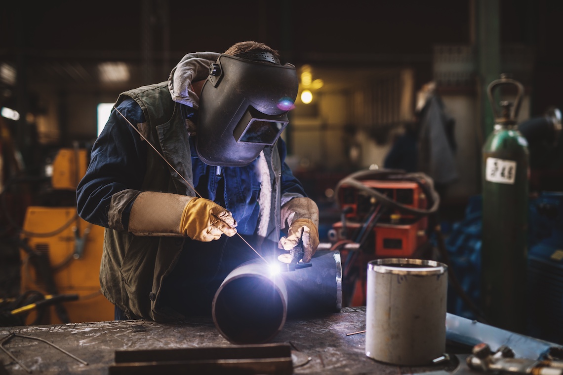 Welder in protective uniform and mask welding metal pipe on the